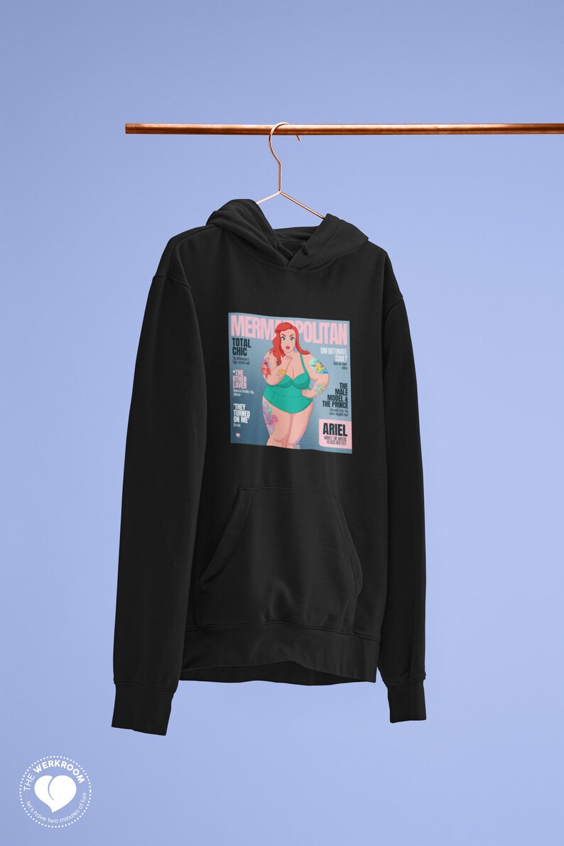 Puede incluir: Sudadera negra con un estampado gr&aacute;fico de una portada de revista que presenta una sirena con cabello rojo y un traje de ba&ntilde;o verde. La portada de la revista se titula "Mermpolitan" y presenta el texto "Total Chic" y "The Male Model & The Prince".