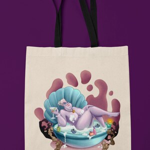 May include: Cream-colored tote bag featuring a cartoon illustration of a purple character lounging in a seashell-shaped tub. The character is holding a cocktail. The bag has black handles and a purple background.