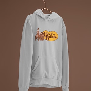 May include: Light gray hoodie with a front pocket and a drawstring hood. The hoodie features a graphic of a person sitting on a stool, playing a barrel organ, with the text "Crack a Bottom" in a brown and yellow oval.