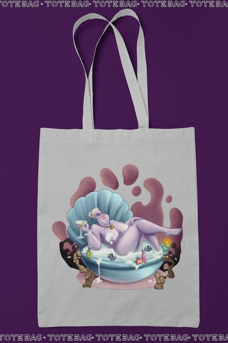 May include: A light gray tote bag featuring a cartoon illustration of a purple character relaxing in a seashell bathtub, holding a cocktail. The bag has white handles and the words "TOTE BAG" repeated at the top and bottom.