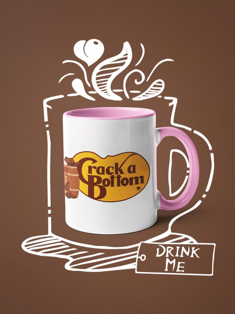 Op de afbeelding: Witte keramische mok met een roze binnenkant en oor. De mok heeft de tekst "Crack a Bottom" in bruin en geel, met een vat-afbeelding. Een witte omtrek van een koffiekopje en de woorden "DRINK ME" zijn ook aanwezig.