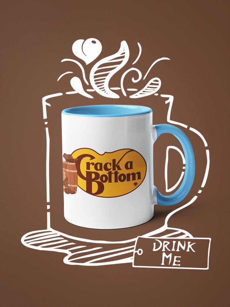 Op de afbeelding: Witte keramische mok met een blauwe binnenkant en handvat. De mok heeft de tekst "Crack a Bottom" in een geel en bruin ovaal ontwerp. Een label met de tekst "DRINK ME" is ook zichtbaar.
