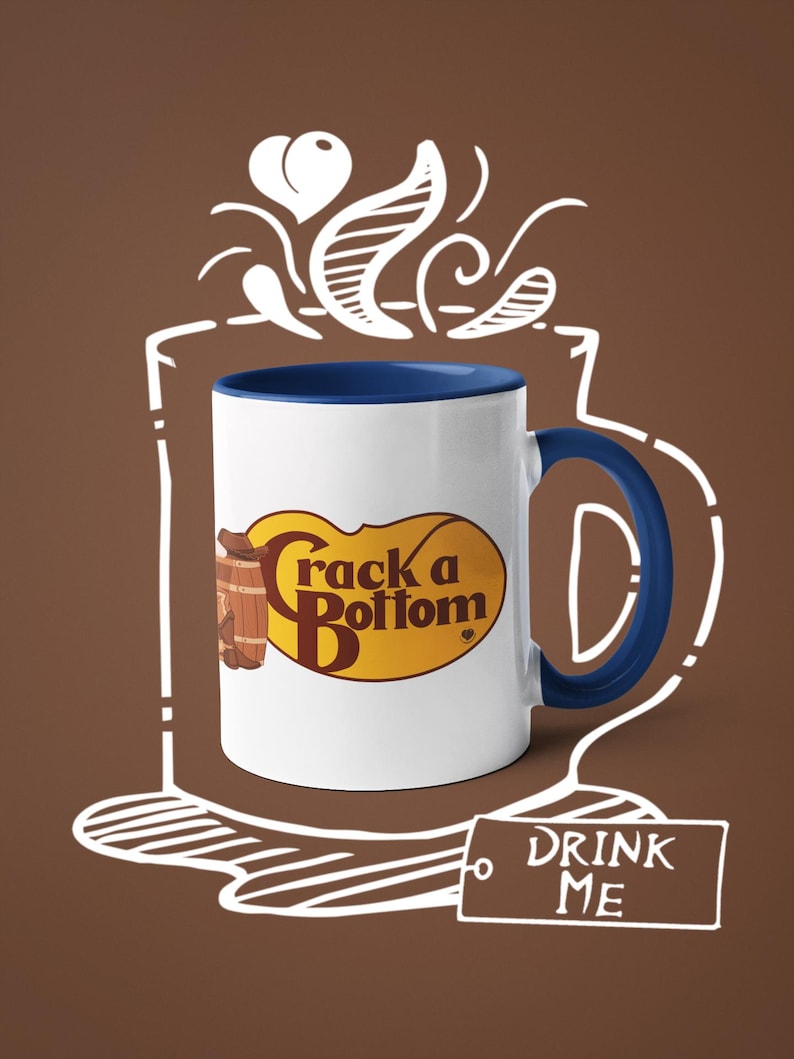 Op de afbeelding: Witte keramische mok met een blauwe binnenkant en handvat. De mok heeft de tekst "Crack a Bottom" in een geel en bruin ovaal ontwerp, met een vat-afbeelding. Een label met "DRINK ME" is ook aanwezig.