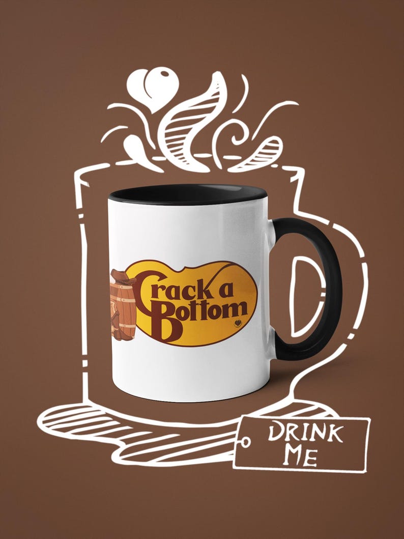 Op de afbeelding: Witte keramische mok met een zwart interieur en handvat. De mok heeft de tekst "Crack a Bottom" in een geel en bruin ovaal ontwerp. Een witte omtrek van een koffiekopje en stoom is rond de mok getekend. Een label met de woorden "DRINK ME" is ook aanwezig.