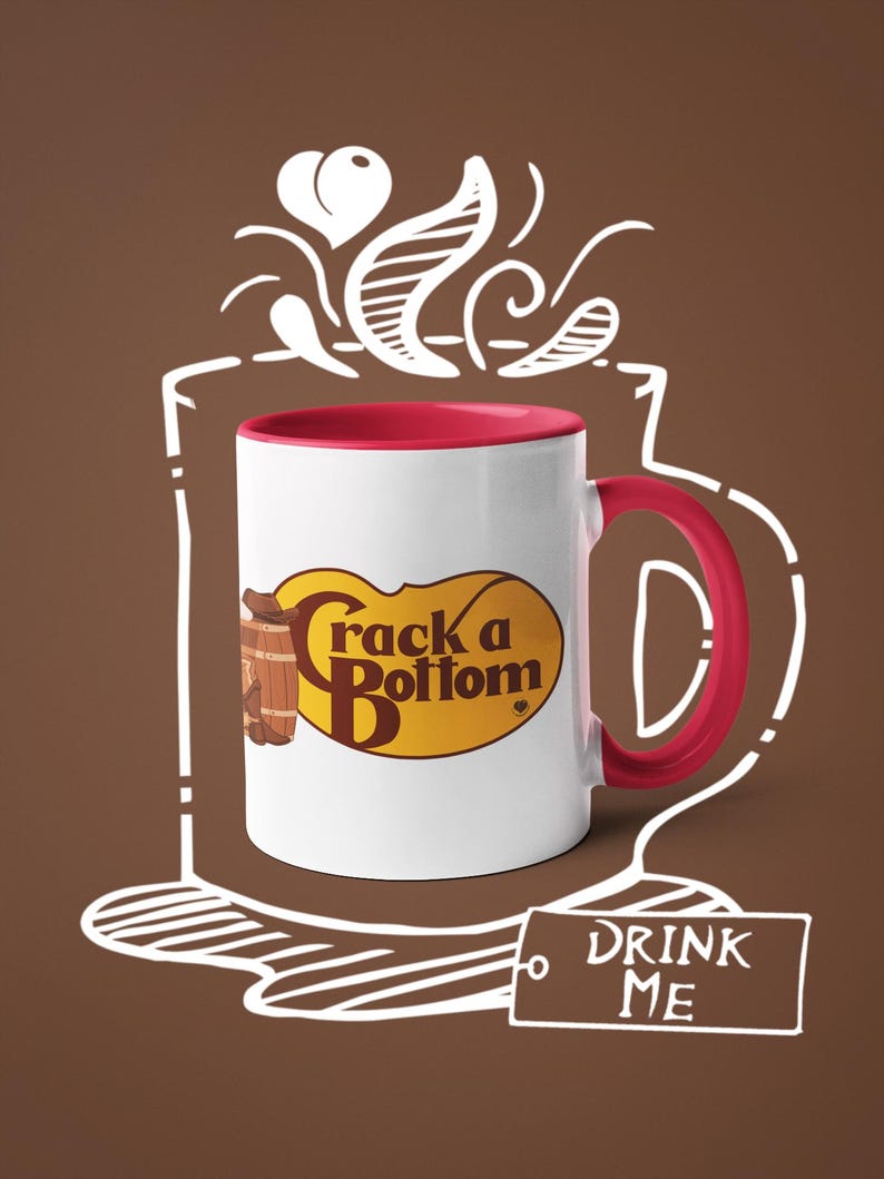 Op de afbeelding: Witte keramische mok met een rode binnenkant en oor. De mok heeft de tekst "Crack a Bottom" in een geel en bruin ovaal ontwerp. Een label met "DRINK ME" staat onder de mok, met een bruine achtergrond en witte omtrek van een kopje.