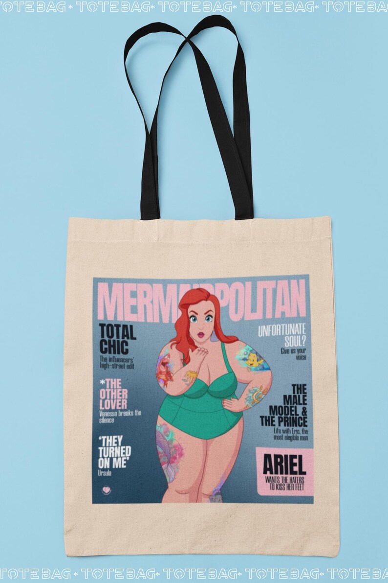 May include: A tote bag with a design of a magazine cover featuring a cartoon mermaid with red hair and tattoos. The magazine cover is titled "Mermopolitan" and features the text "Total Chic", "The Other Lover", "They Turned On Me", "Unfortunate Soul?", "The Male Model & The Prince", and "Ariel Wants The Haters To Kiss Her Feet".