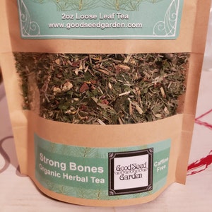 May include: A brown paper bag with a green and white label that reads "Promotes: Nutrient Dense Healthy Bones 2oz Loose Leaf Tea www.goodseedgarden.com". The bag contains a blend of dried herbs and the label on the front reads "Strong Bones Organic Herbal Tea Good Seed Garden Caffeine Free".