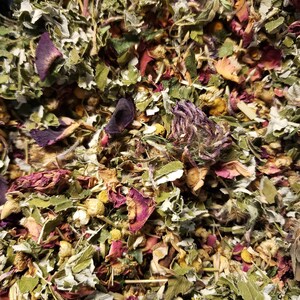 May include: A close-up of a mixture of dried herbs and flowers, including green leaves, purple petals, and yellow flowers.