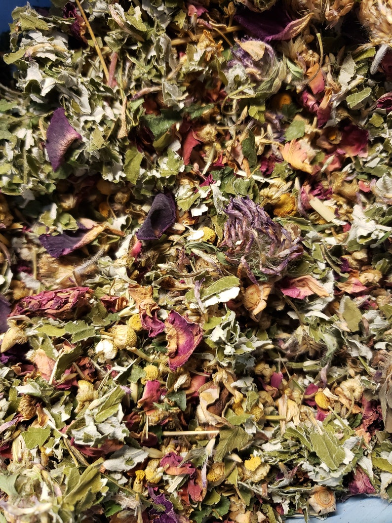 May include: A close-up of a mixture of dried herbs and flowers, including green leaves, purple petals, and yellow flowers.