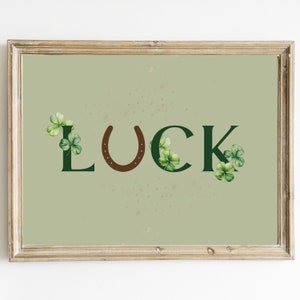 May include: A framed print with a green background and the word "LUCK" in green letters with a brown horseshoe in between the "U" and "C".  There are green shamrocks around the letters.