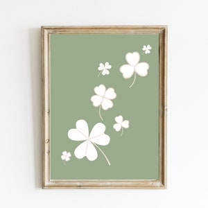 May include: A framed print with a green background and white four-leaf clover designs. The clovers are scattered across the print in a random pattern.