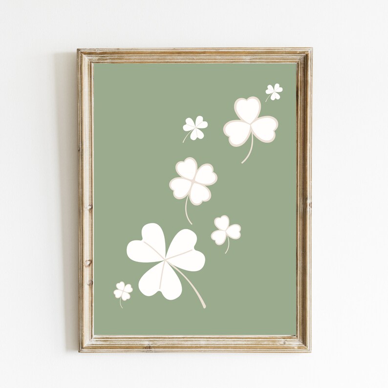 May include: A framed print with a green background and white four-leaf clover designs. The clovers are scattered across the print in a random pattern.