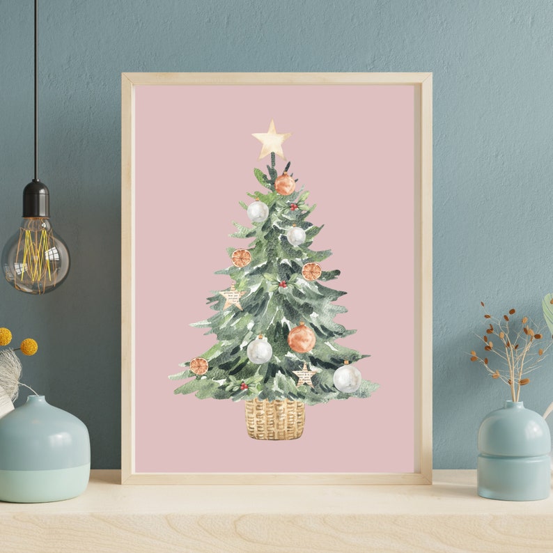 K&ouml;nnte beinhalten: Ein Aquarellbild eines Weihnachtsbaums vor rosa Hintergrund. Der Baum ist mit wei&szlig;en und orangefarbenen Kugeln, einem Stern oben und einem braunen Weidenkorb geschm&uuml;ckt.