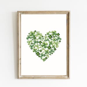 Op de afbeelding: Een ingelijste print met een hartvorm gemaakt van groene klavers. Het kunstwerk staat tegen een witte achtergrond en de lijst heeft een lichtbruine afwerking. De afbeelding roept het thema van St. Patrick's Day op.