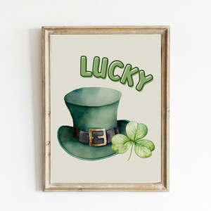May include: A printable art print with a green leprechaun hat and a four-leaf clover. The text "LUCKY" is written in green letters.