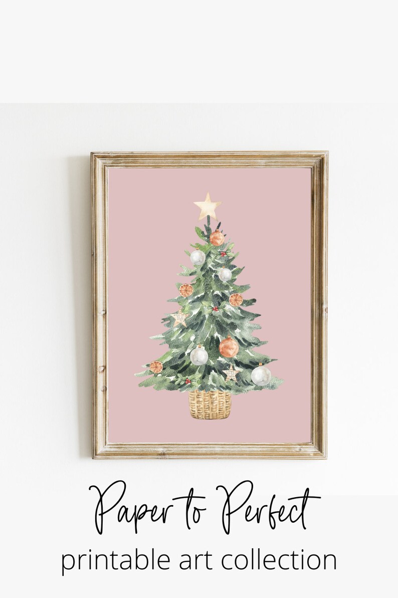 K&ouml;nnte beinhalten: Ein Aquarellbild eines Weihnachtsbaums vor rosa Hintergrund. Der Baum ist mit wei&szlig;en und orangen Kugeln, einem goldenen Stern oben und einem Korb an der Basis geschm&uuml;ckt. Der Text "Paper to Perfect printable art collection" befindet sich unter dem Bild.