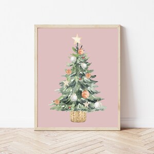 K&ouml;nnte beinhalten: Ein Aquarellbild eines Weihnachtsbaums vor rosa Hintergrund. Der Baum ist mit wei&szlig;en und orangefarbenen Kugeln, einem goldenen Stern oben und einem Weidenkorb geschm&uuml;ckt.