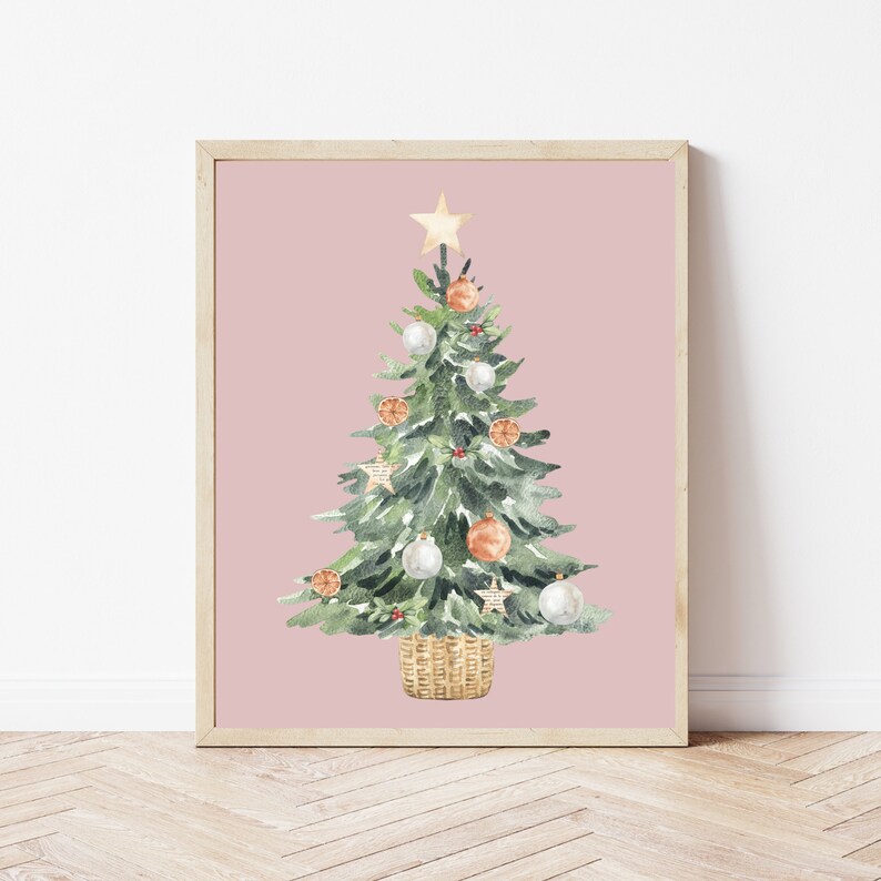 K&ouml;nnte beinhalten: Ein Aquarellbild eines Weihnachtsbaums vor rosa Hintergrund. Der Baum ist mit wei&szlig;en und orangefarbenen Kugeln, einem goldenen Stern oben und einem Weidenkorb geschm&uuml;ckt.
