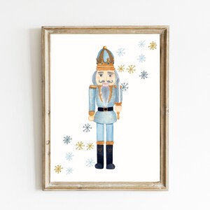 May include: A watercolor illustration of a blue and gold nutcracker soldier with a crown and a sword. The background is white with blue and gold snowflakes.