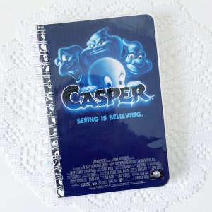 以下が含まれることがあります： カスペル・ザ・フレンドリー・ゴーストの映画ポスターデザインが施された、青と黒のスパイラルバインディングノート。表紙にはカスペルと他の3人の幽霊が描かれており、「カスペル」と「見ることは信じること」の文字が書かれている。