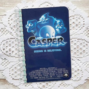 以下が含まれることがあります： カスペル・ザ・フレンドリー・ゴーストの映画ポスターデザインが施された青いスパイラルバインディングノート。表紙にはカスペルと3人の幽霊の兄弟が、「カスペル」と「見ることは信じること」の文字と共に描かれています。