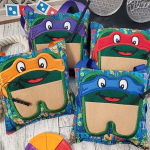 May include: Four Teenage Mutant Ninja Turtles themed fabric bags with different colored masks, each with a felt mask and a small pocket. A colorful pizza toy is in the foreground. Decorative items are in the background.