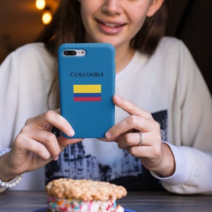 Puede incluir: Una funda de tel&eacute;fono azul con la palabra "Colombia" y la bandera colombiana. La funda se sostiene frente a un postre, un s&aacute;ndwich de helado con chispas, en un plato azul.