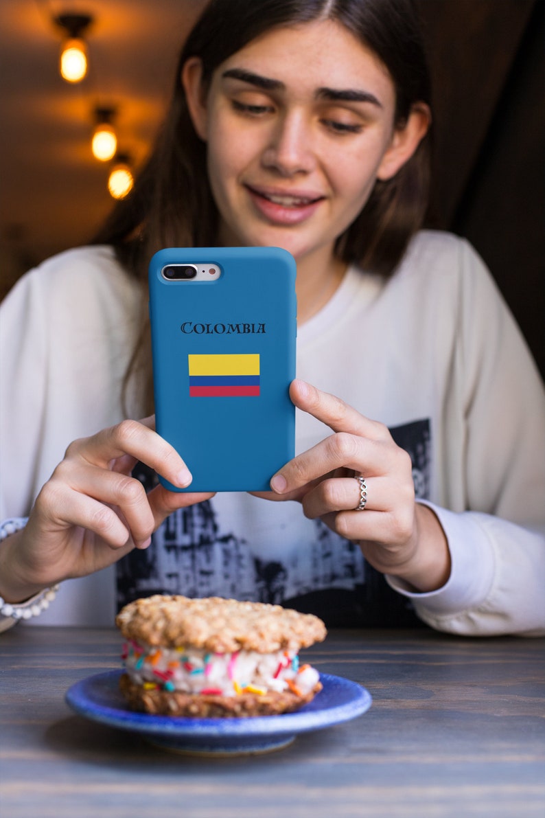 Puede incluir: Una funda de tel&eacute;fono azul con la palabra "Colombia" y la bandera colombiana. La funda se sostiene frente a un postre, un s&aacute;ndwich de helado con chispas, en un plato azul.