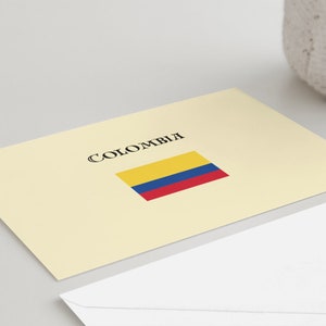 Puede incluir: Una tarjeta color crema con la palabra "COLOMBIA" en escritura negra sobre una bandera rectangular amarilla, azul y roja. Un sobre blanco est&aacute; en primer plano.