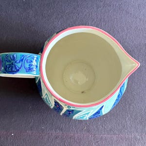 K&ouml;nnte beinhalten: Keramikkrug mit Henkel, verziert mit einem floralen Muster in Blau und Wei&szlig;. Der Rand ist rosa umrandet. Der Innenraum ist cremefarben.