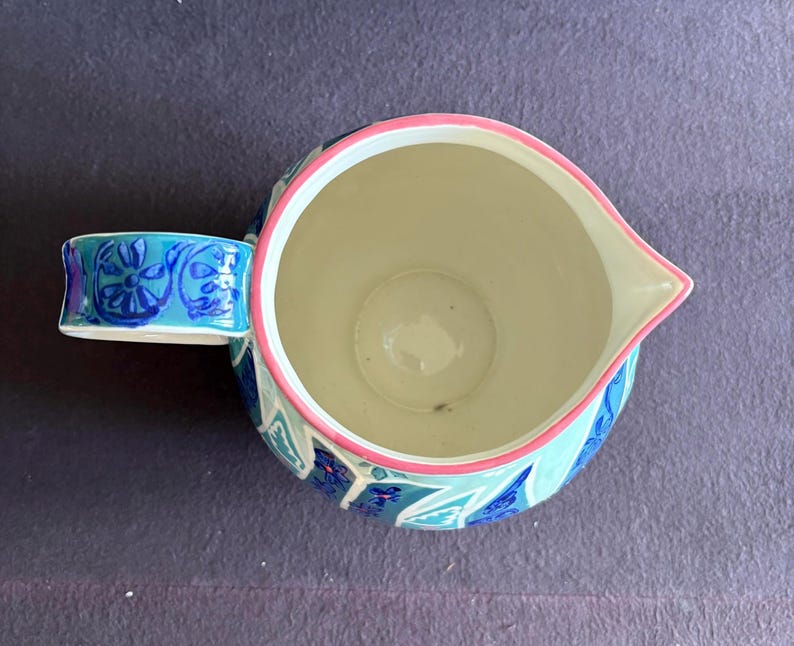 K&ouml;nnte beinhalten: Keramikkrug mit Henkel, verziert mit einem floralen Muster in Blau und Wei&szlig;. Der Rand ist rosa umrandet. Der Innenraum ist cremefarben.
