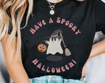 May include: A black t-shirt with a pink graphic of a ghost holding a pumpkin and a broom. The text "Have a Spooky Halloween!" is written in a pink circle around the ghost.