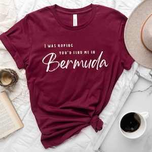 Puede incluir: Una camiseta de color granate con texto blanco que dice "Esperaba que me encontraras en Bermuda".
