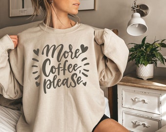 May include: A beige sweatshirt with the text "More Coffee, Please" in brown lettering with hearts and swirls around the text.