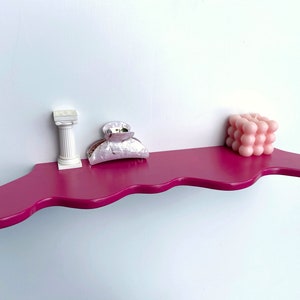 May include: A pink wavy shelf with a white column, a pink bubble candle, and a white and silver hair clip.
