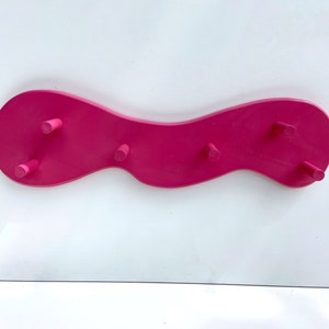 May include: A pink wooden wall-mounted coat rack with a wavy design and five hooks.
