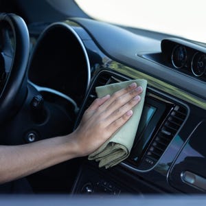 以下が含まれることがあります： 人の手が、薄い緑色のマイクロファイバークロスを使って車の内部を掃除しています。クロスは、ダッシュボードとセンターコンソールを拭くために使用されています。