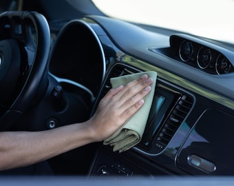 May include: A person's hand cleaning the interior of a car with a light green microfiber cloth. The cloth is being used to wipe down the dashboard and center console.