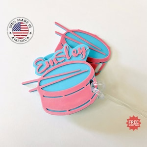 May include: Pink and blue plastic luggage tag shaped like a drum with the name "Emley" written on it.