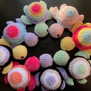 May include: A collection of nine crocheted sea turtle toys in various colors, including pink, yellow, green, blue, and purple. Each turtle has a different colored shell and a black face.