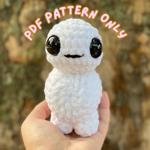 May include: White crocheted amigurumi toy with large black eyes and a smiling mouth. The toy is being held in a hand. The text "PDF PATTERN ONLY" is written in orange letters above the toy.