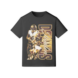 May include: A black t-shirt featuring a vintage-style graphic of football players in action. The design includes the name "Daniels" in a stylized font, with a gold and brown color scheme. The shirt is a classic crew neck.