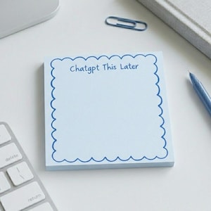 以下が含まれることがあります： 「ChatGPT This Later」の文字が入った、波型の縁取りのある水色の付箋の束。キーボード、ペン、クリップ、ノートも写っています。