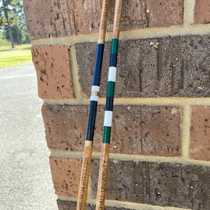 May include: Two wooden walking sticks with black, white, and green stripes. One stick has "PITTSBURGH STEELERS" printed on it, and the other says "MARSHALL UNIVERSITY". Both sticks have "TODD PRIDEMORE" printed on them.