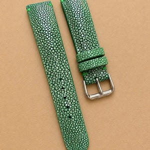 May include: A bright green watch strap with a textured stingray skin pattern and visible green stitching. The strap features a silver-toned metal buckle and two matching keepers. The text RioBebeStore is printed in red in the upper left corner.