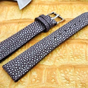 May include: A dark purple watch strap featuring a textured stingray skin pattern with small, rounded, light-colored bumps across the surface. The strap includes a silver-toned metal buckle and a matching sliding loop for secure fastening.