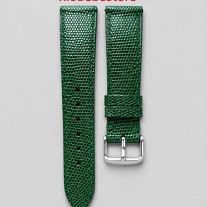 Puede incluir: Una correa de reloj de dos piezas en color verde esmeralda con un patrón texturizado de piel de lagarto. La correa cuenta con una hebilla de metal plateado y dos trabillas verdes a juego. El texto RioBebeStore aparece impreso en rojo.
