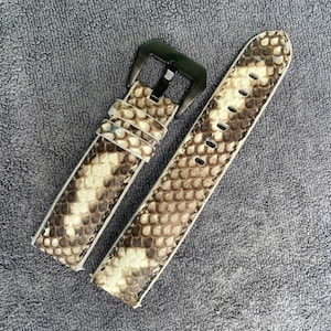 May include: A watch strap featuring a textured snakeskin pattern in shades of beige, brown, and cream. The strap includes a dark metallic buckle and two matching leather keepers, showcasing a detailed scale design across the entire surface.