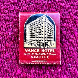 May include: A vintage matchbook cover featuring a black and white illustration of the Vance Hotel in Seattle, Washington. The text on the cover reads "Vance Hotel, Clive W. McDonald, Manager, Seattle, Made in U.S.A., The Diamond Match Co Chico Calif."