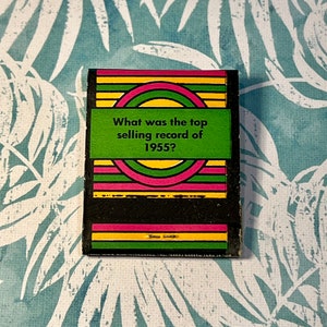 May include: A green, yellow, and pink striped card with a black circle in the center. The card asks "What was the top selling record of 1955?"